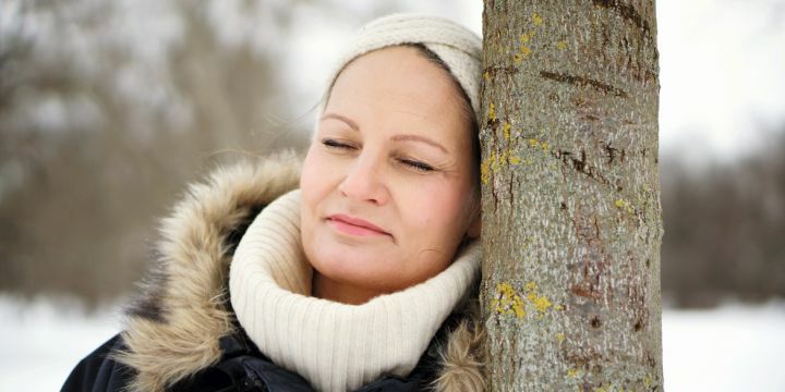Frau an Baum lehnend im Winter mit Schal und Haarband