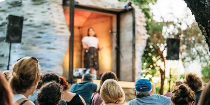 Auftritt Frau auf Bühne im Folly im Hintergrund, vorn Köpfe von Gästen