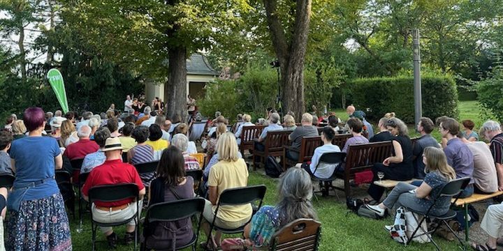 Konzert im Garten, viele Menschen sitzend, Band im Hintergrund