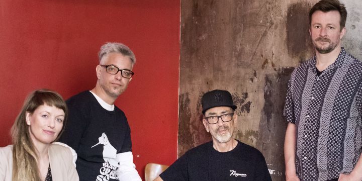 4 Personen stehend uns sitzend, frontal, eine Frau, drei Männer, bunt