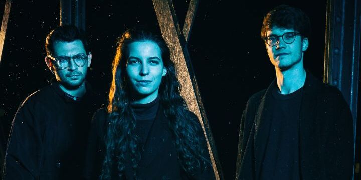 Trio Porträt Oberkörper, schwarze Kleidung, blau-weiße Gesichter, zwei Männer mit Brille, eine Frau mit langen Haaren