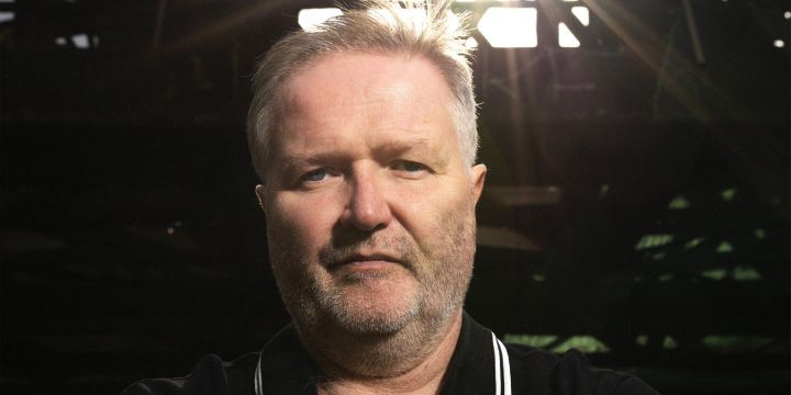 Mann im schwarzen Polo-Shirt, graue, kurze Haare, blaue Augen, leichter Bartwuchs