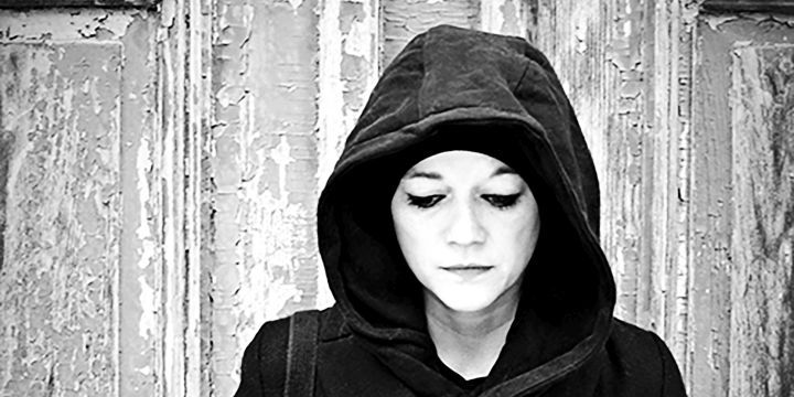 Frau vor einer alter Tür, hat eine Kapuze über dem Kopf, Blick nach unten gerichtet, schwarz-weiß Foto